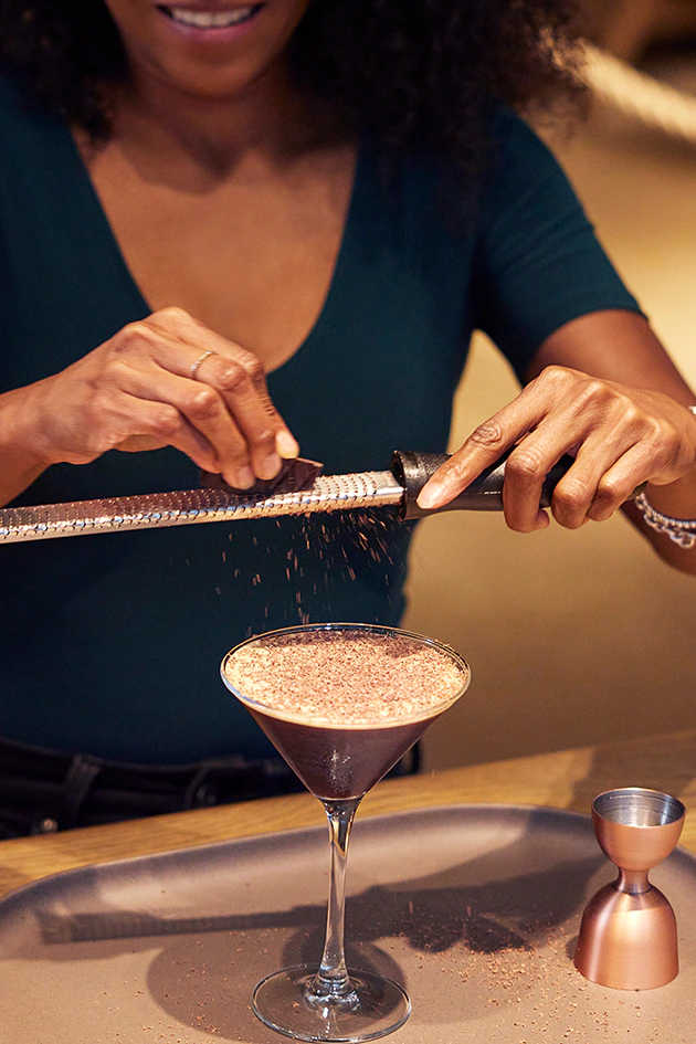 Woman grates chocolate over martini.