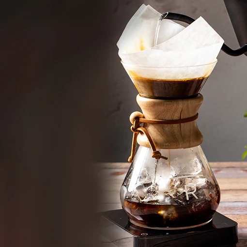 Water pours from a gooseneck kettle into a Chemex brewer.
