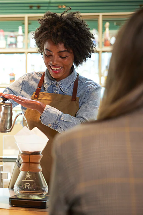 A woman pours from a gooseneck kettle into a Chemex coffee brewer.