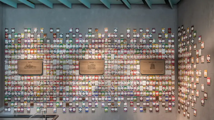 Display of hundreds of colorful Starbucks Reserve coffee cards in a grid on the wall with wooden plaques about each Starbucks Reserve Roastery interspersed