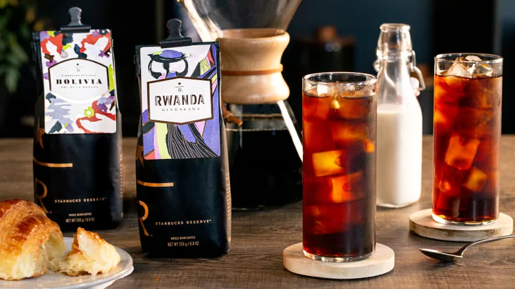 Two bags of coffee alongside two glasses of iced coffee.