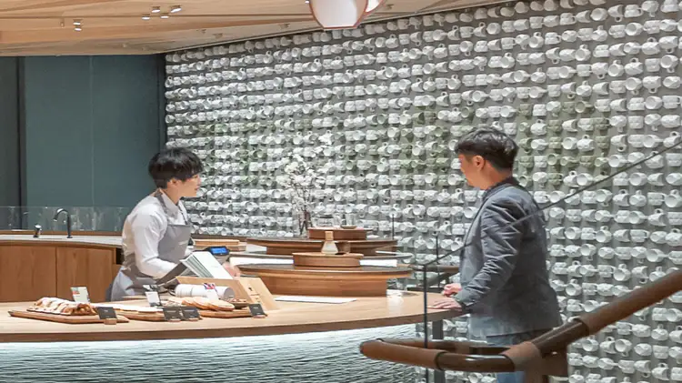 A rectangular art piece made of 2,300 Teavana tea cups attached to a wall, with "TEAVANA" spelled out within, and Teavana barista and customer in foreground