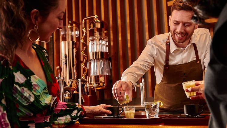 A bartender pours a beverage for a smiling customer.