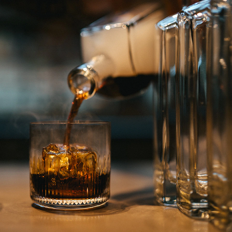 A cocktail being poured from a glass bottle.