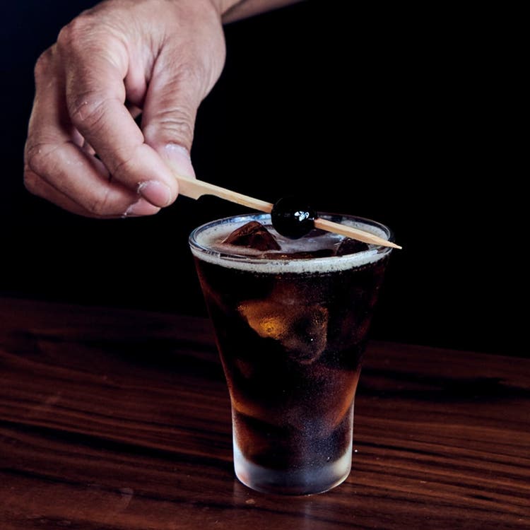 A cocktail being garnished with a cherry on a skewer.