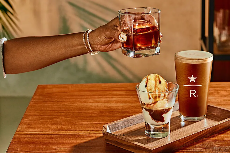 A hand picks up an iced coffee from a table, where a nitro coffee and affogato are sitting on a tray.