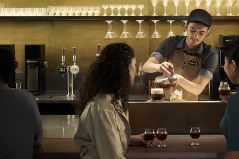 A bartender making drinks while two people sitting at the counter watch.