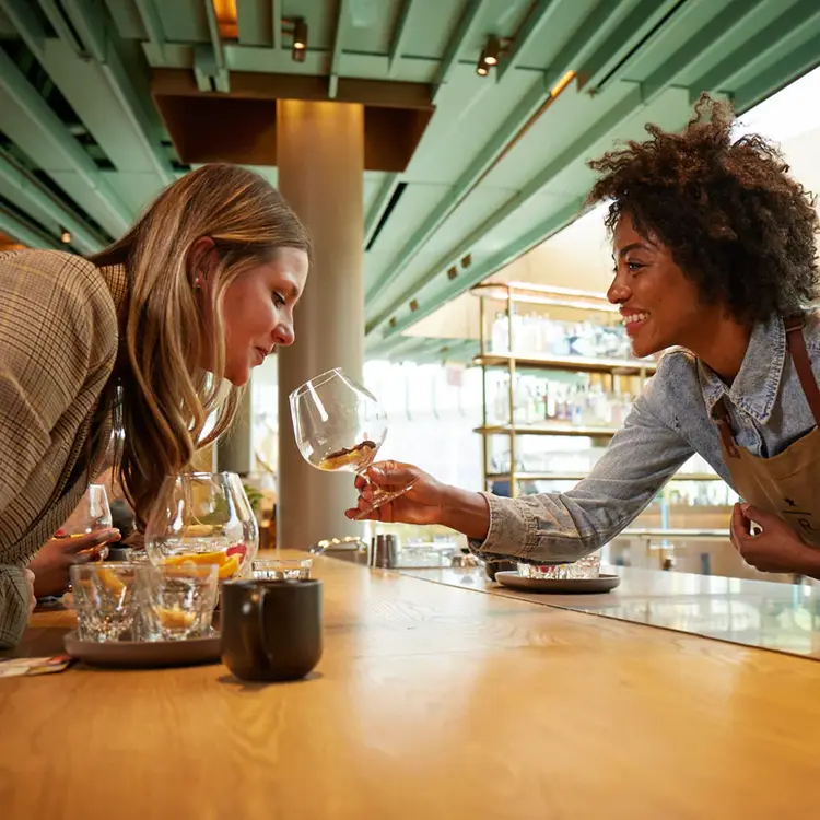 Woman holds out a snifter glass with aromatic components while another woman leans forward to smell the glass.