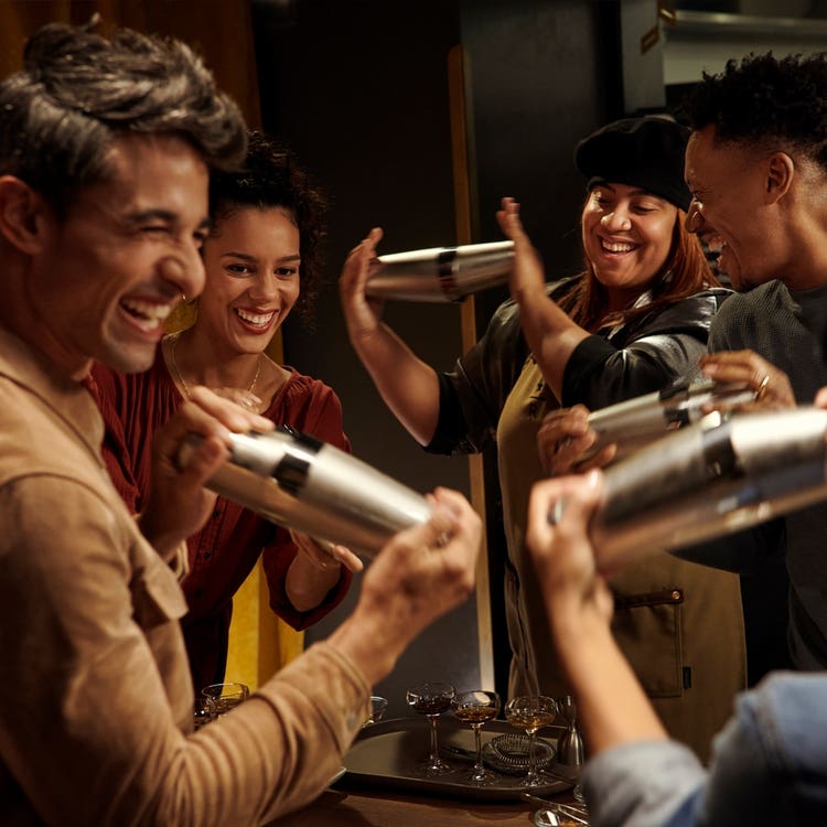 A group of people smiling and shaking cocktails in metal cocktail shakers.