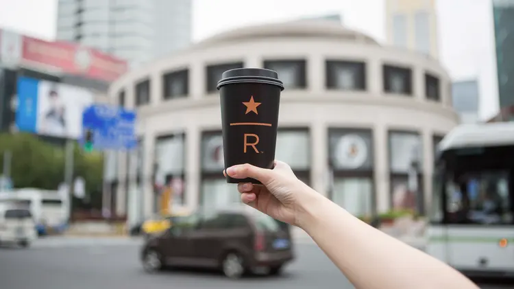 A cup of Starbucks Reserve coffee held in the air, within a city scene.